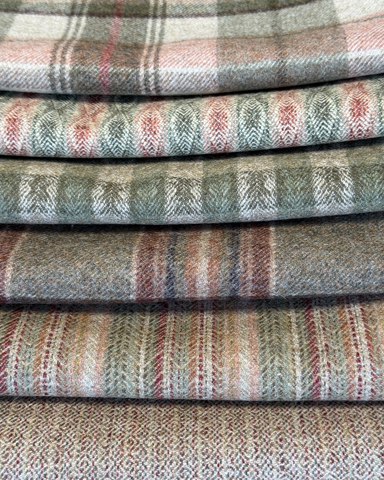 Utvalg av tekstiler fra Moon Heritage II i lune, dempede fargetoner, med klassiske ruter, striper og vevde mønstre i grønt, beige, rust og grått. Serien består av 100 % ull og viser hvordan ulike mønstre og nyanser kan kombineres i en helhetlig tekstilpalett. Fra Eventyrlig Oppussing Naustdal. Foto.