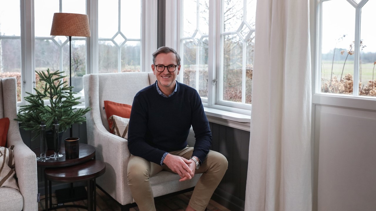 Halvor Bakke sitter i lenestol på sin glassveranda med mange vinduer og lyse gardiner på småbruket på Trae. Foto.