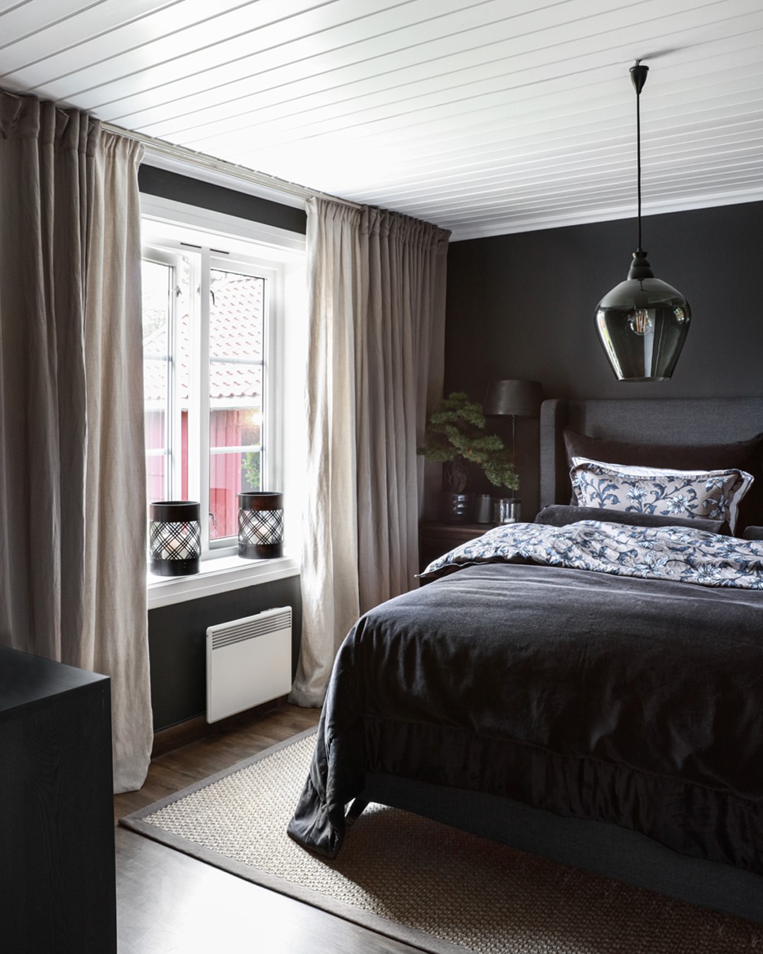 Halvor Bakkes soverom med mørke vegger, dobbeltseng og vinduer med hvite doble gardinskinner og to lag med gardiner. Foto.