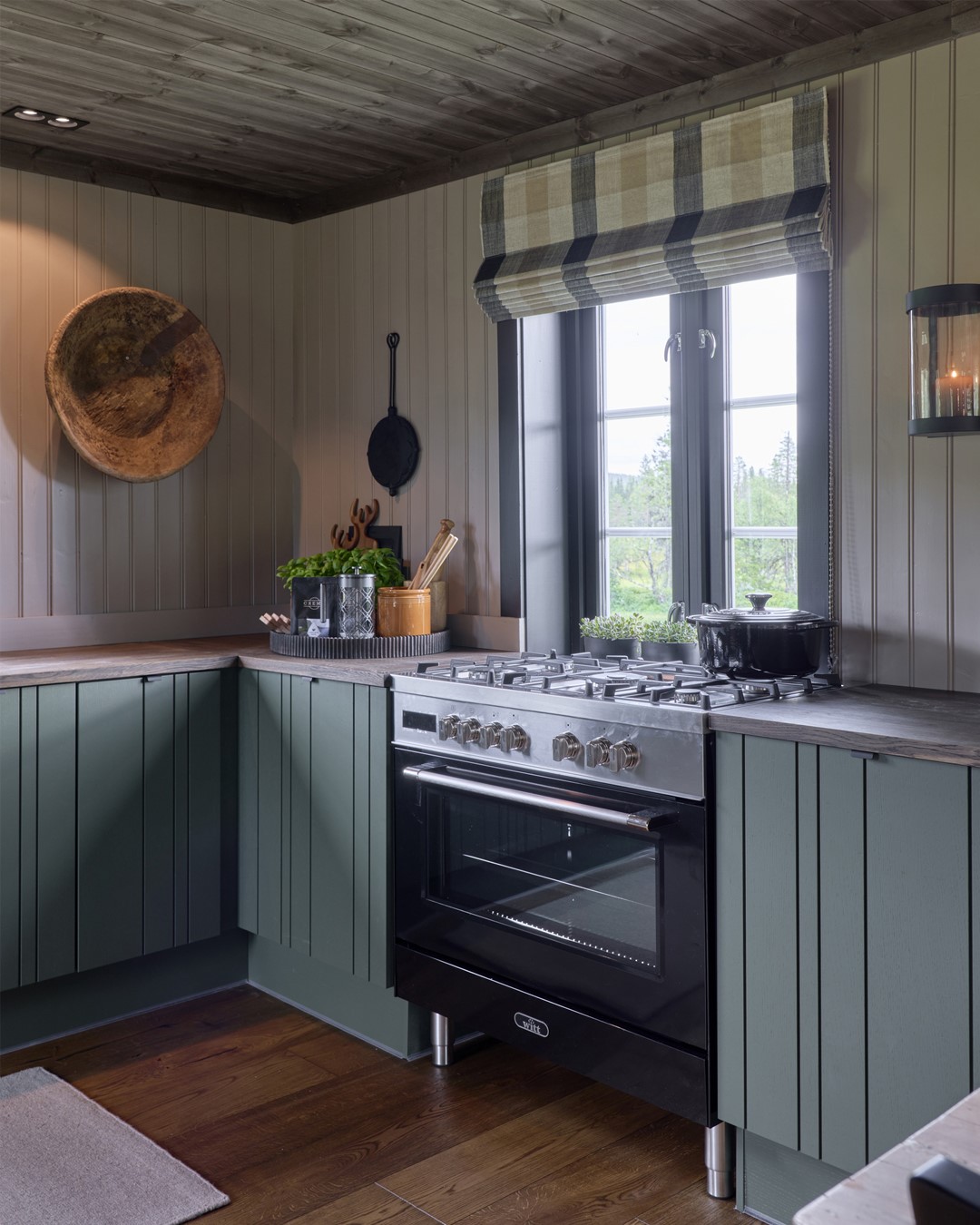 Kjøkken med malte grønne fronter. Beige panelvegger. Vindu over kjøkkenbenk med sorte malte lister. Skreddersydd liftgardin i rutete tekstil fra Ian Mankin. Mørkt tregulv og tak. Fra Eventyrlig Oppussing 2025, Snåsa. Foto. Kjøkken med malte grønne fronter. Beige panelvegger. Vindu over kjøkkenbenk med sorte malte lister. Skreddersydd liftgardin i rutete tekstil fra Ian Mankin. Mørkt tregulv og tak. Fra Eventyrlig Oppussing 2025, Snåsa. Foto.