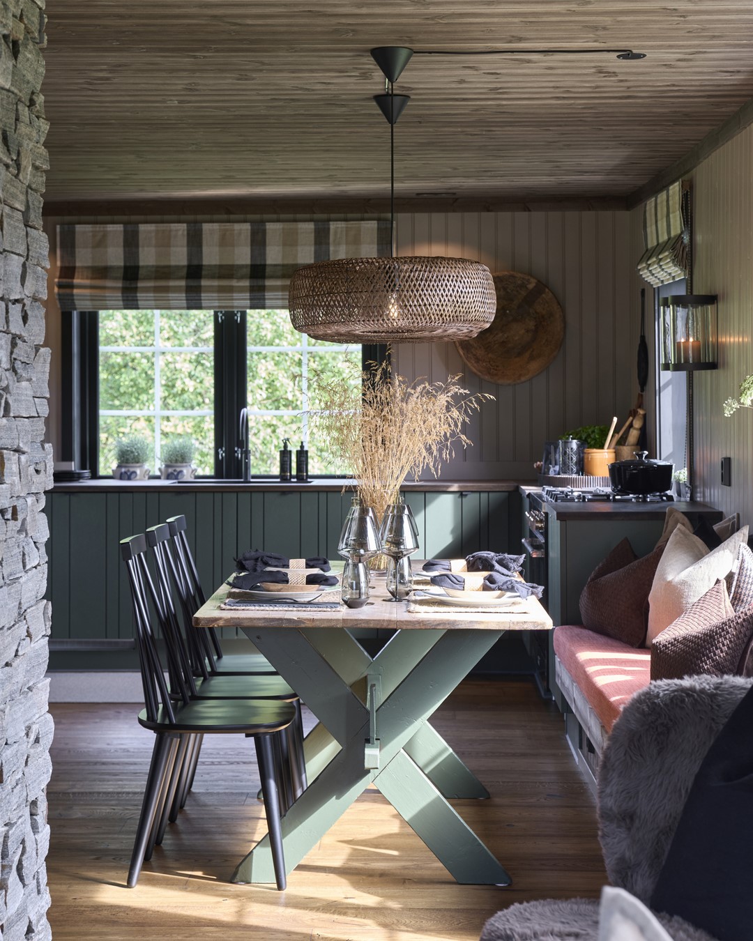 Spisestue og kjøkken fra hytta i Almoseteren. Kjøkkenfronter i grønt. Vindu over kjøkkenbenk med sorte malte lister. Skreddersydd liftgardin i rutete tekstil fra Ian Mankin. Oppdekket spisebord. Sittebenk under vindu med teracotta farget madrass og store puter. Trestoler. Beige vegger og mørkt tregulv og tak. To store flettede taklamper over spisestuen. Fra Eventyrlig Oppussing 2025, Snåsa. Foto. Spisestue og kjøkken fra hytta i Almoseteren. Kjøkkenfronter i grønt. Vindu over kjøkkenbenk med sorte malte lister. Skreddersydd liftgardin i rutete tekstil fra Ian Mankin. Oppdekket spisebord. Sittebenk under vindu med teracotta farget madrass og store puter. Trestoler. Beige vegger og mørkt tregulv og tak. To store flettede taklamper over spisestuen. Fra Eventyrlig Oppussing 2025, Snåsa. Foto.
