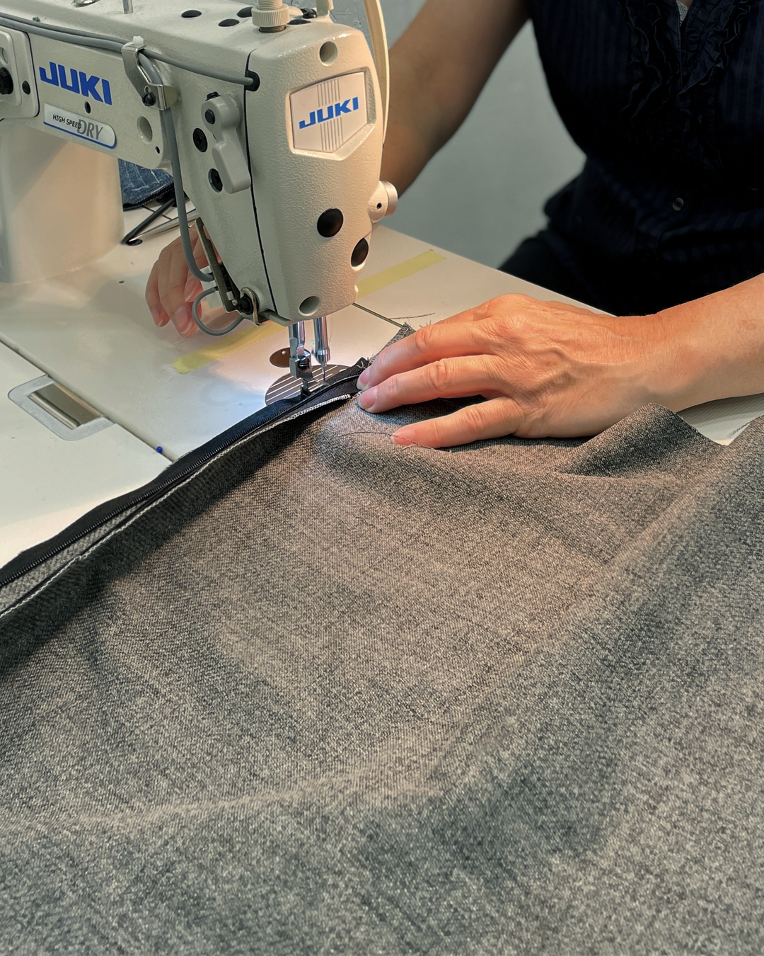 Fra Gardinmaker sømstudio ser vi en symaskin og et tekstil som sys av en sømmerske. Foto.
