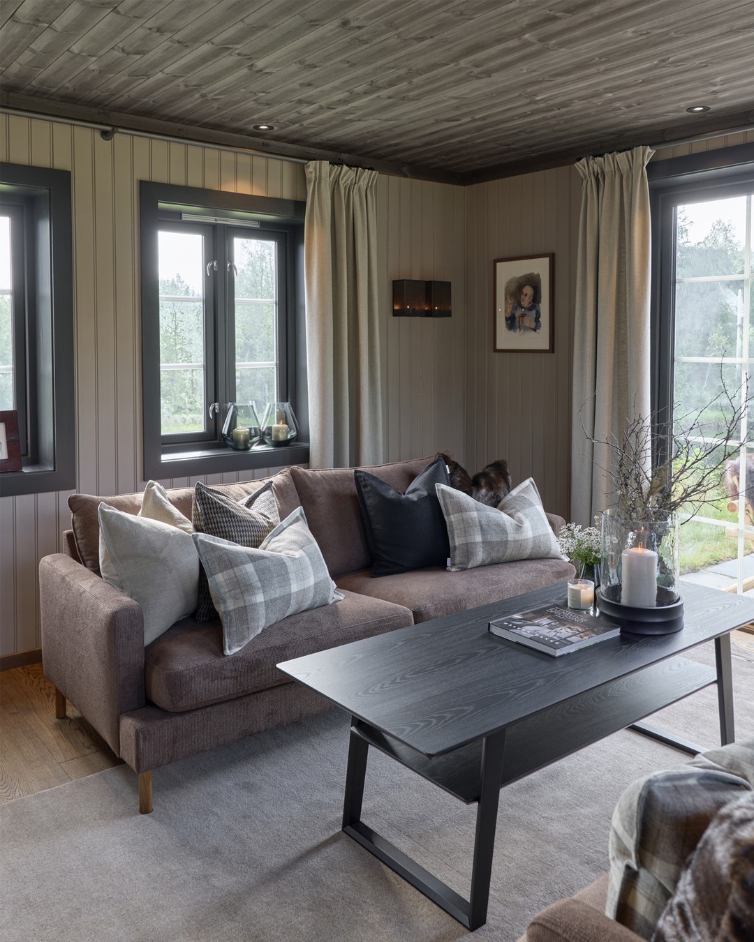 Stua på Almoseteren. Varmt tregulv og tak. Lyse vegger. Vindu med sortemalte lister. Dus plommefarget sofa med puter i ulike tekstiler of farger. Sort sofabord med blomster, kvister og lyslykter. Gulvteppe i lys beige farge. Fra Eventyrlig Oppussing 2025, Almoseteren i Snåsa. Foto. Stua på Almoseteren. Varmt tregulv og tak. Lyse vegger. Vindu med sortemalte lister. Dus plommefarget sofa med puter i ulike tekstiler of farger. Sort sofabord med blomster, kvister og lyslykter. Gulvteppe i lys beige farge. Fra Eventyrlig Oppussing 2025, Almoseteren i Snåsa. Foto.