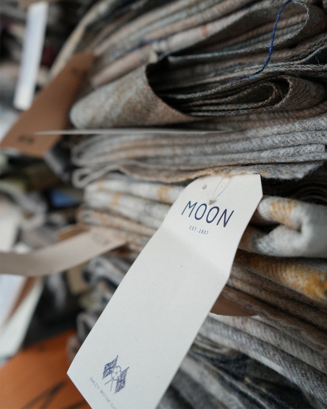 Detaljbilde av Moon ull-tekstiler som ligger stablet i hyllen klar til bruk, sømstudio hos Gardinmaker.no. Foto. Detaljbilde av Moon ull-tekstiler som ligger stablet i hyllen klar til bruk, sømstudio hos Gardinmaker.no. Foto.