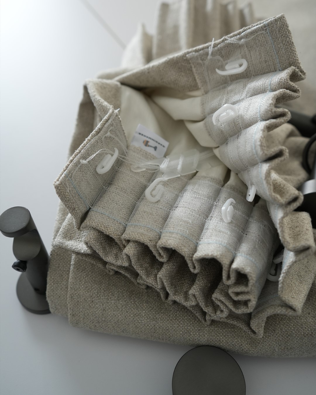 Detaljbilde av gardinhøyde med blyantfold og kroker. Skreddersydd gardin i tekstilen Kyri fra Roma, i fargen Taupe. Madison gardinstang i fargen Matt Graphite. Fra sømstudio hos Gardinmaker.no. Foto. Detaljbilde av gardinhøyde med blyantfold og kroker. Skreddersydd gardin i tekstilen Kyri fra Roma, i fargen Taupe. Madison gardinstang i fargen Matt Graphite. Fra sømstudio hos Gardinmaker.no. Foto.