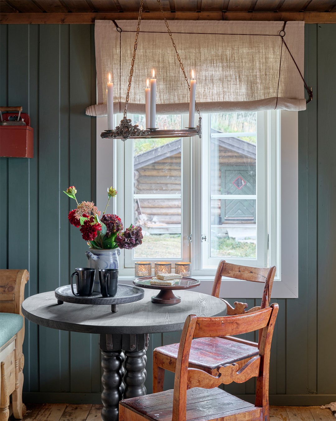 Lys, skreddersydd liftgardin i naturfarget tekstil over vinduet ved spiseplassen, med synlige snorer og dekorative ringer som understreker det rustikke uttrykket i rommet. Fra Eventyrlig Oppussing Mesnali. Foto.