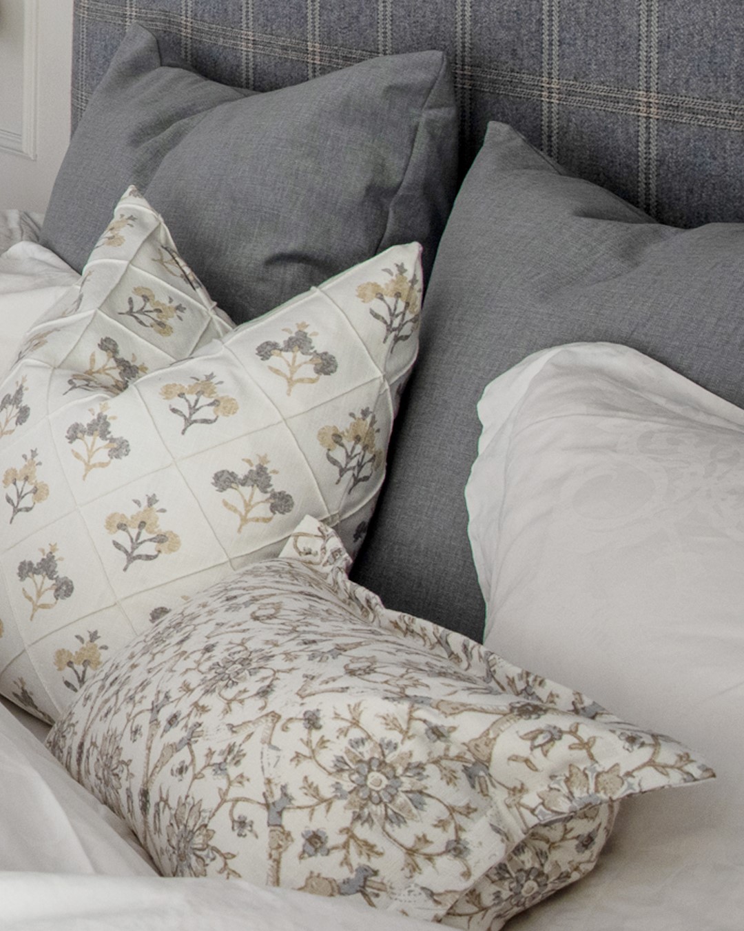 Detaljbilde av puter i ulike størrelser og mønster i seng på soverom med hotellfølelse. Foto.