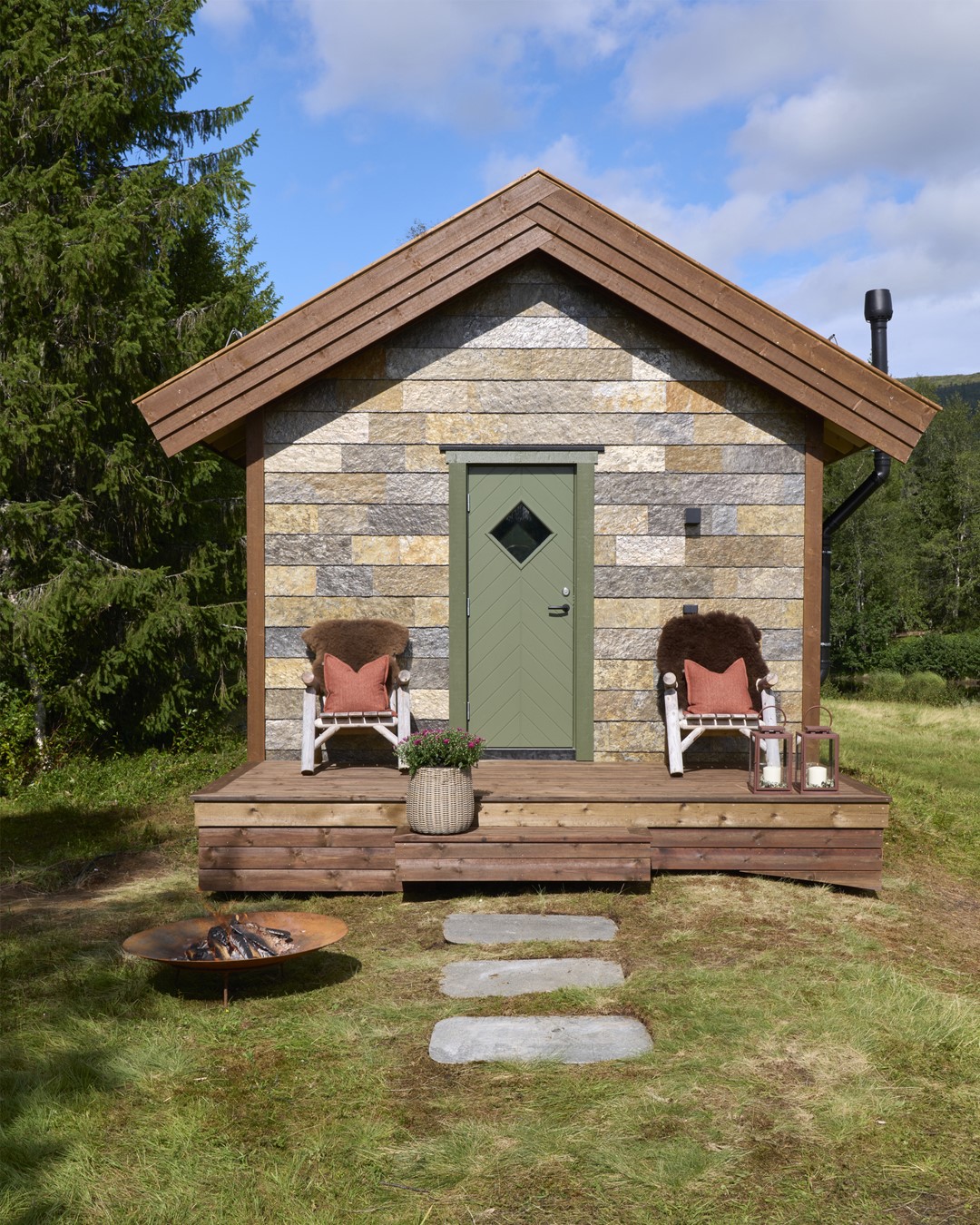 Bilde av annekset fra utsiden. Skiferstein på fasaden. Rødbrun beis på takutstikk. Og platting. Mosegrønn inngangsdør med vindu. Store stoler med skinn og puter på hver side av inngangsdøren. Fra Eventyrlig Oppussing 2025, Almoseteren i Snåsa. Foto. Bilde av annekset fra utsiden. Skiferstein på fasaden. Rødbrun beis på takutstikk. Og platting. Mosegrønn inngangsdør med vindu. Store stoler med skinn og puter på hver side av inngangsdøren. Fra Eventyrlig Oppussing 2025, Almoseteren i Snåsa. Foto.